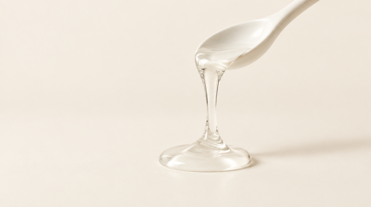 Gel transparente que cae de una cuchara de cerámica sobre un fondo crema
