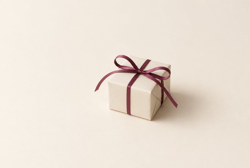 Caja de regalo envuelta en papel crema con un lazo de seda burdeos sobre fondo crema